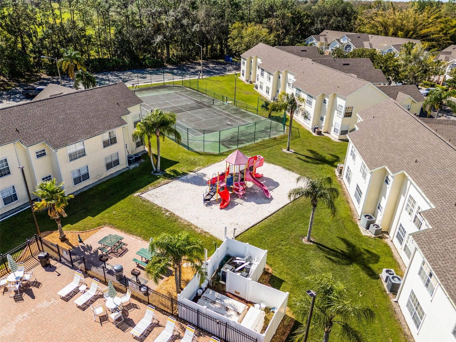 5017 LAGUNA BAY CIRCLE, #100, Kissimmee, FL 34746 Outdoor Recreational Areas: Focused aerial view showcasing the community playground structure, picnic/grilling zone, fenced tennis court, and manicured green grounds.