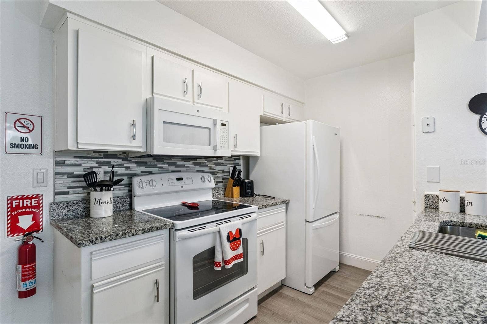 5017 LAGUNA BAY CIRCLE, #100, Kissimmee, FL 34746 Kitchen Interior: Bright kitchen equipped with clean white cabinetry, granite countertops, a mosaic tile backsplash, electric range, and matching white appliances.