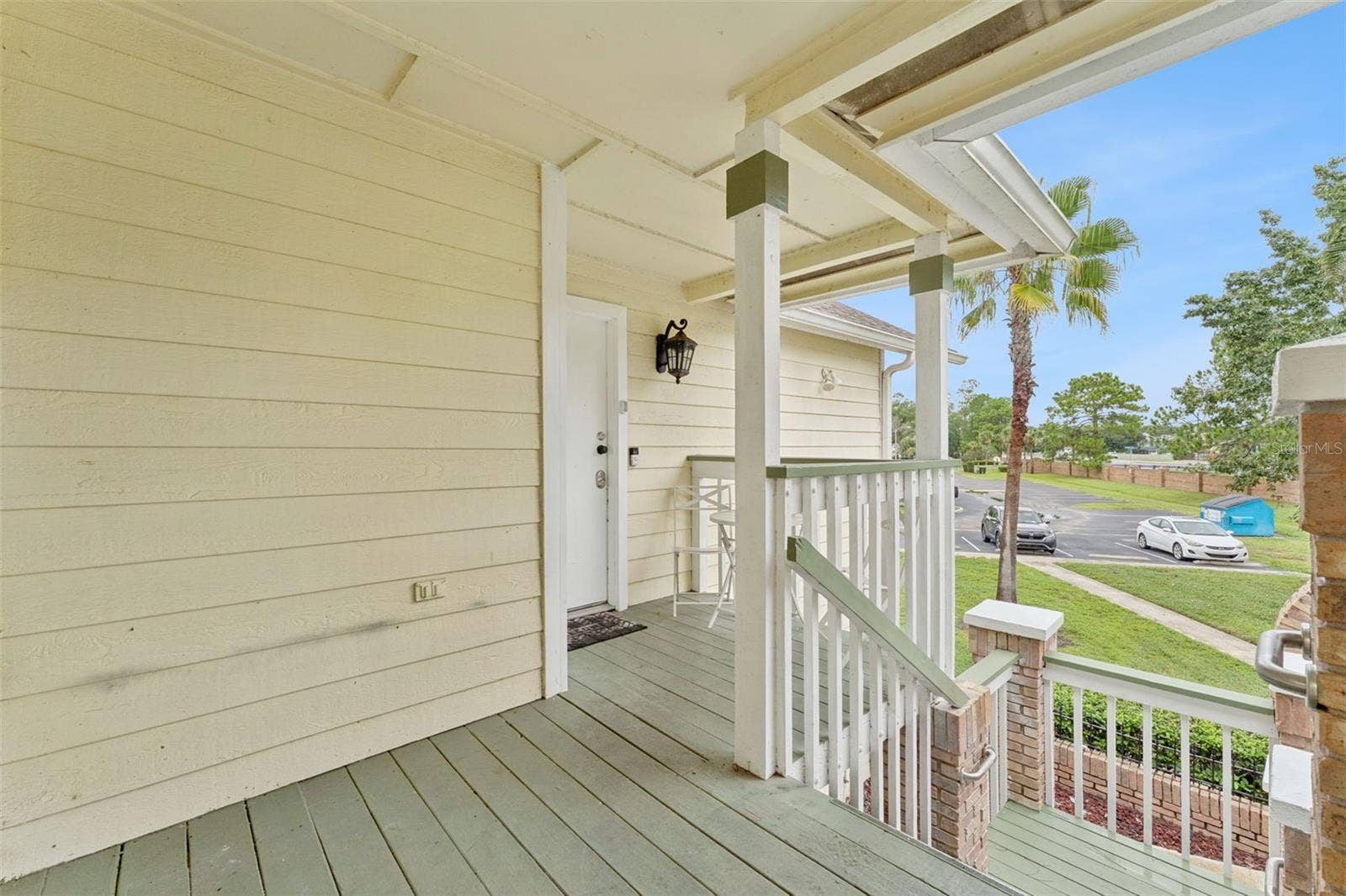 5017 LAGUNA BAY CIRCLE, #100, Kissimmee, FL 34746 Covered Entry Deck: Covered front porch featuring painted wood decking, classic railing, brick column accents, and entry lighting