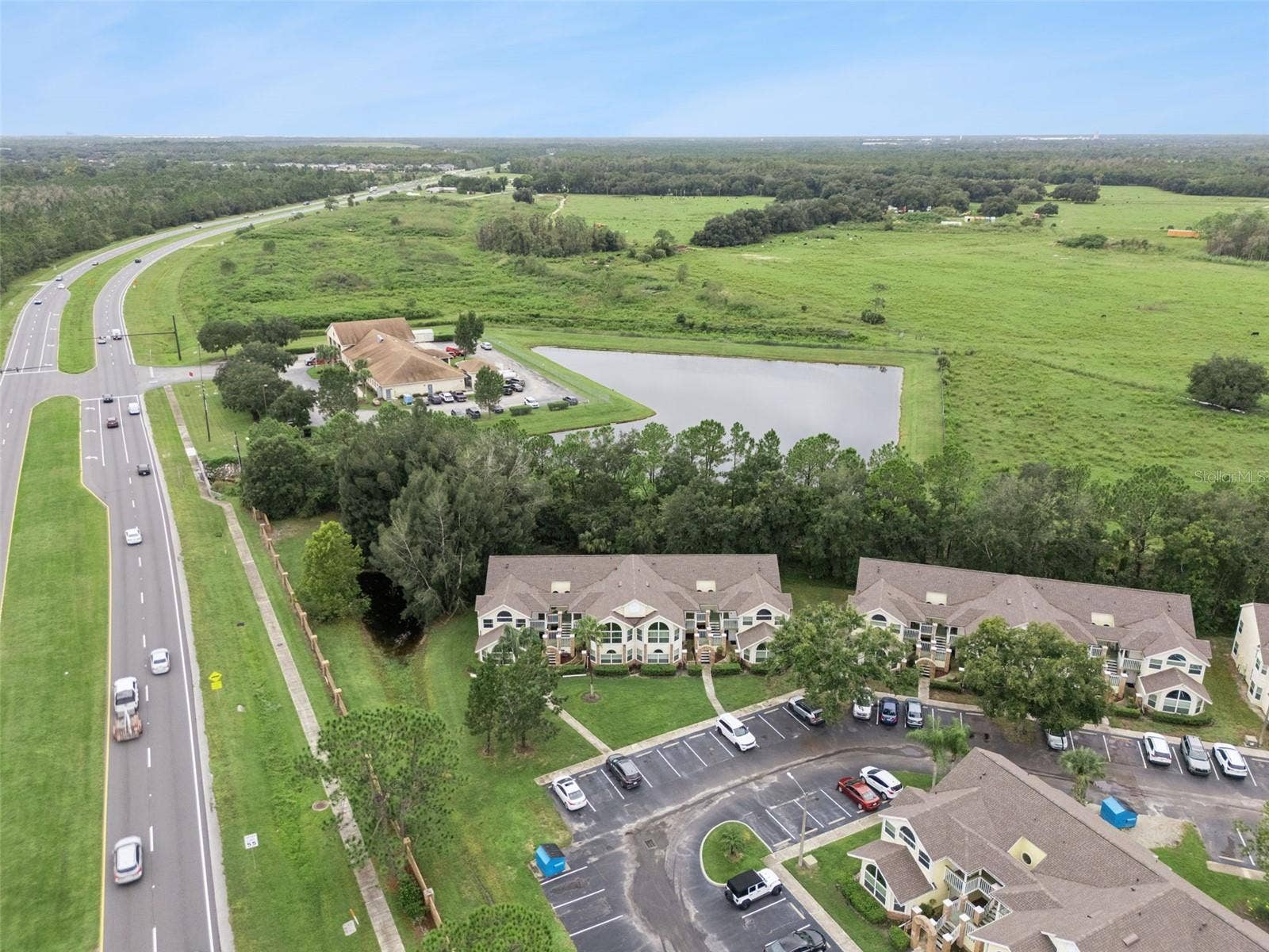 5017 LAGUNA BAY CIRCLE, #100, Kissimmee, FL 34746 Community & Pond Overview: Broad aerial panorama displaying the condominium grounds, nearby water feature, surrounding open green spaces, and adjacent thoroughfare.