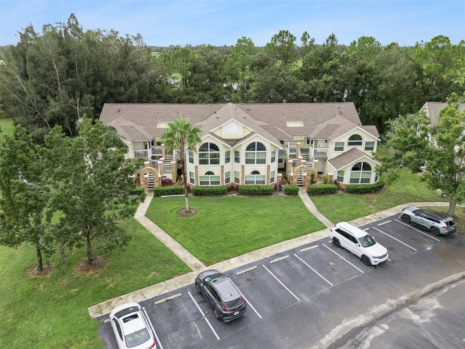 5017 LAGUNA BAY CIRCLE, #100, Kissimmee, FL 34746 Exterior Aerial Perspective: Front aerial view displaying the building facade, brick architectural entries, central palm landscaping, and parking lot