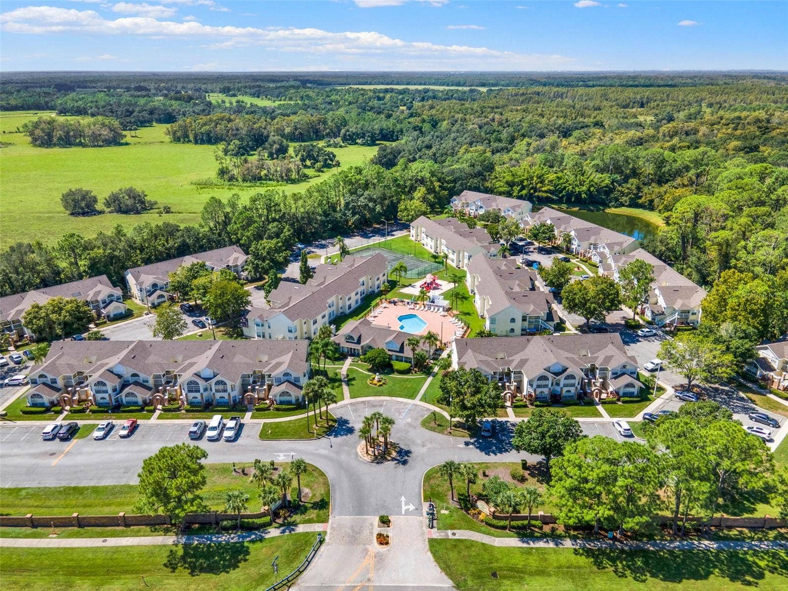 5017 LAGUNA BAY CIRCLE, #100, Kissimmee, FL 34746 Community Entrance & Layout Aerial: Broad aerial view capturing the main entrance roundabout, central pool deck, clubhouse, tennis court, and residential layout.