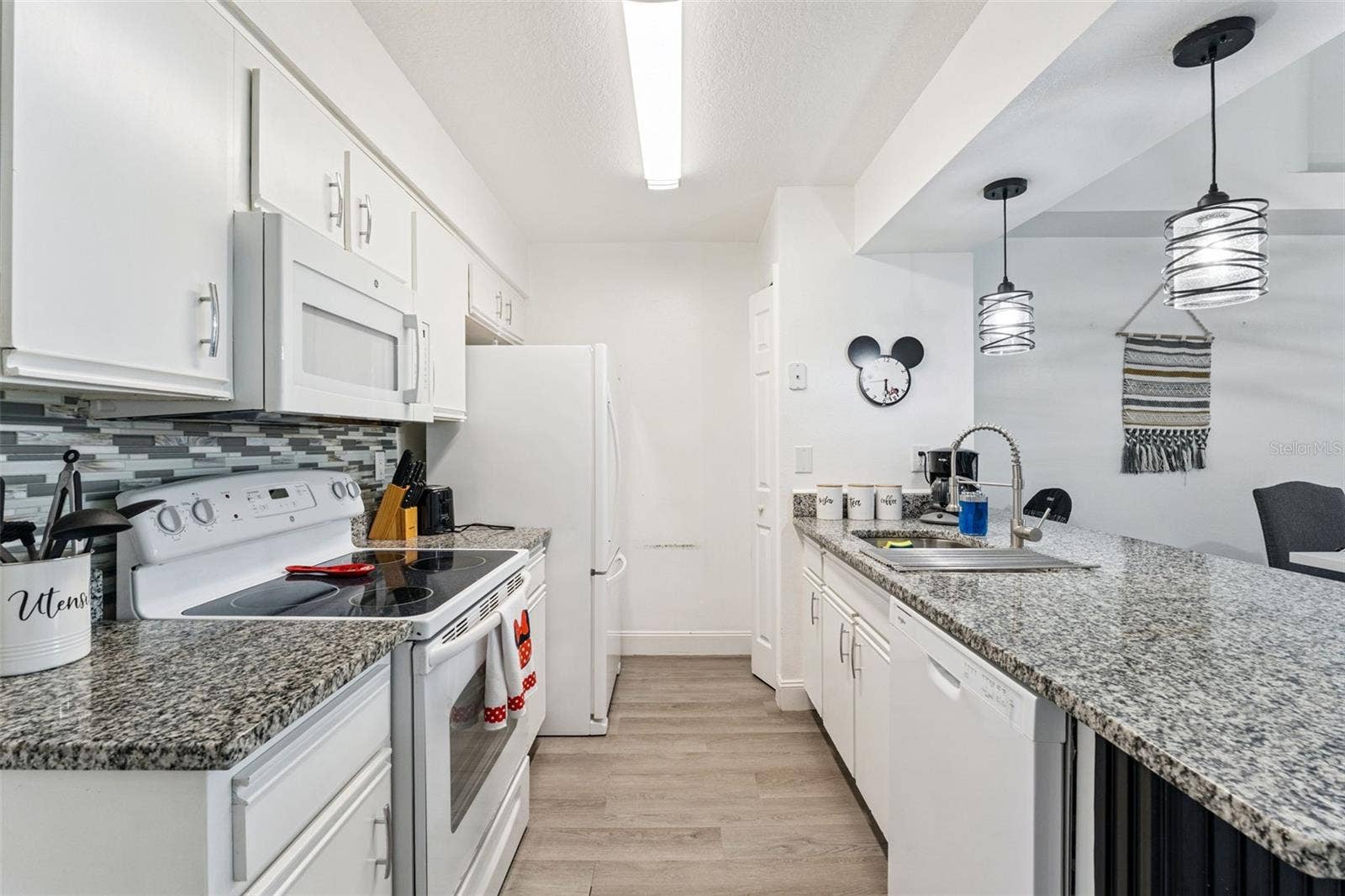 5017 LAGUNA BAY CIRCLE, #100, Kissimmee, FL 34746 Kitchen & Breakfast Bar: Kitchen perspective highlighting durable granite counters, undermount sink with goose-neck faucet, dishwasher, and modern pendant lights over the peninsula.