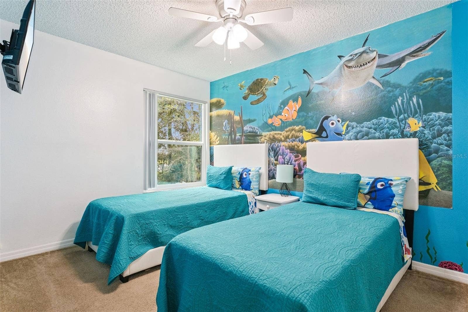 5017 LAGUNA BAY CIRCLE, #100, Kissimmee, FL 34746 Underwater-Themed Twin Bedroom: Fun themed guest bedroom with dual twin beds, vibrant ocean wall mural, ceiling fan, carpet flooring, and wall-mounted TV.