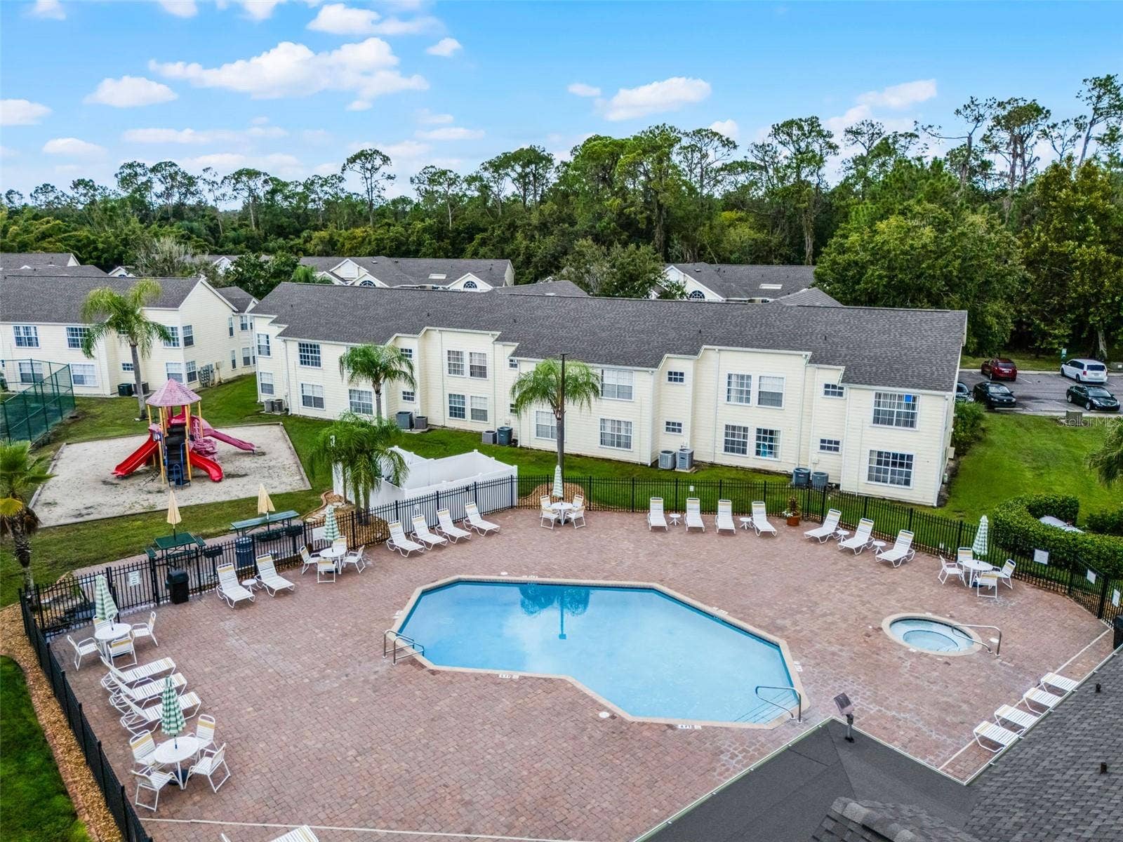 5017 LAGUNA BAY CIRCLE, #100, Kissimmee, FL 34746 Resort Pool & Playground View: Angled drone view of the paver pool deck, integrated hot tub, lounge seating, fenced perimeter, and adjacent children's playground.