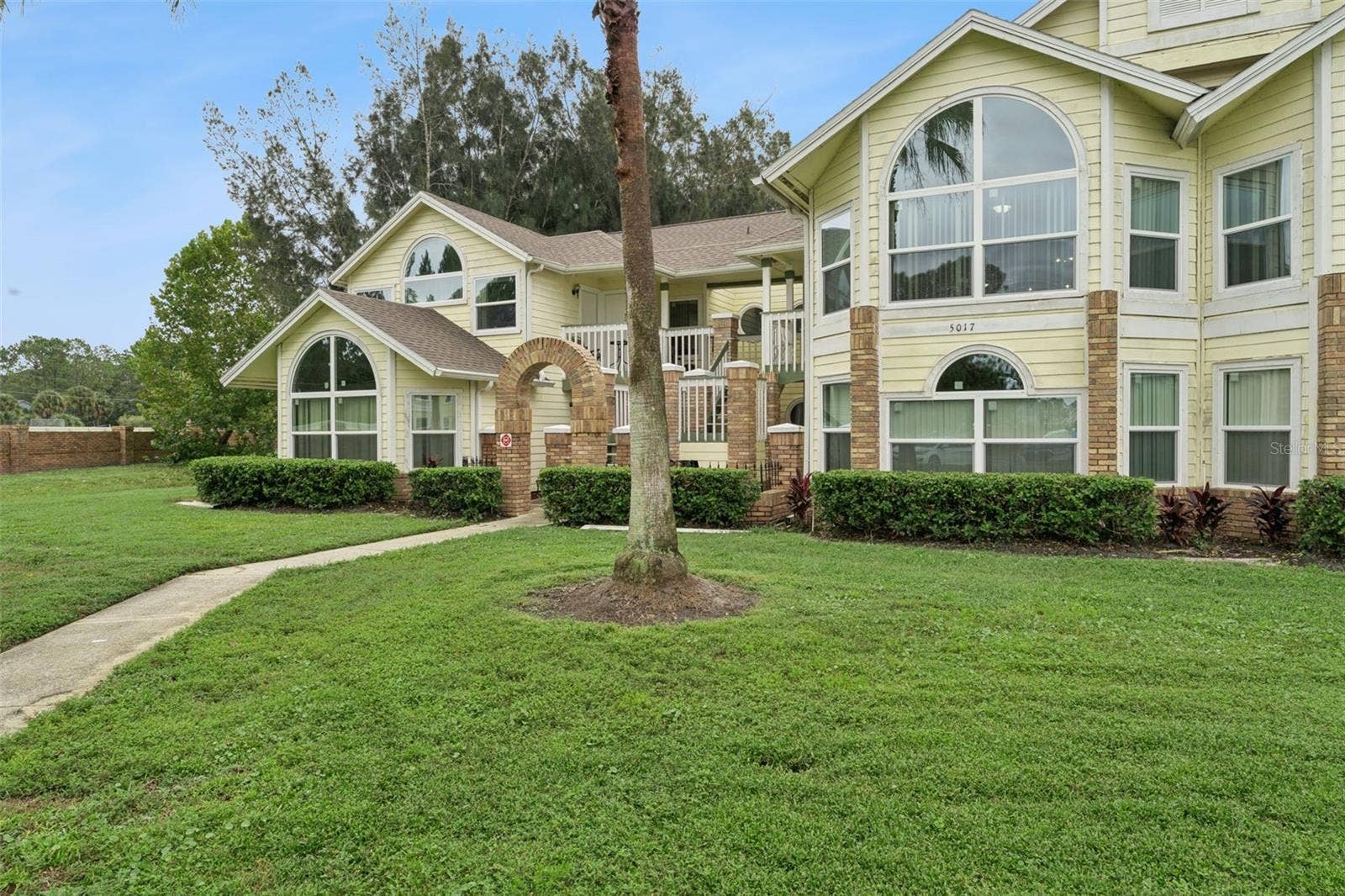 5017 LAGUNA BAY CIRCLE, #100, Kissimmee, FL 34746 Front Walkway & Entry: Paver walkway leading up to the brick entry archway, framed by mature palm trees and green space.