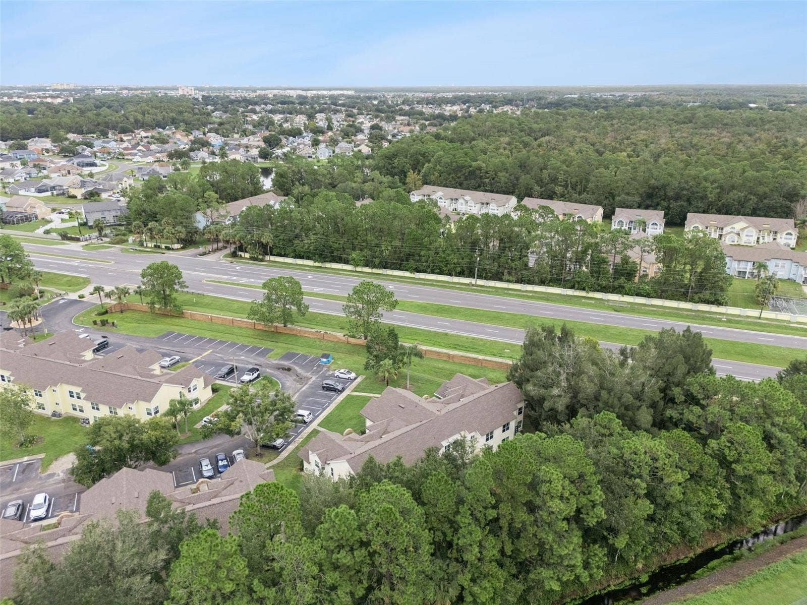 5017 LAGUNA BAY CIRCLE, #100, Kissimmee, FL 34746 High-Angle Regional Aerial: Elevated drone view displaying the building nestled beside a lush pine tree buffer, showing parking access, surrounding neighborhoods, and convenient proximity to major roadways.