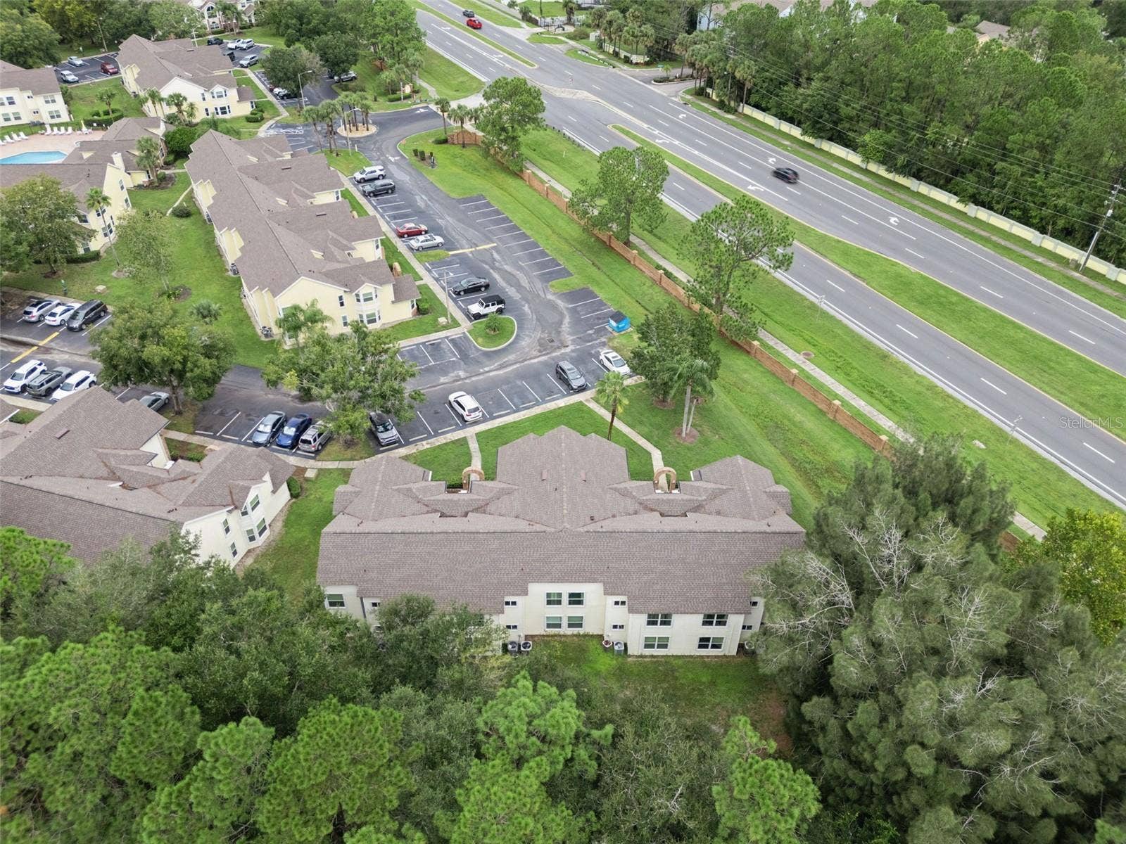 5017 LAGUNA BAY CIRCLE, #100, Kissimmee, FL 34746 Aerial View of Rear & Grounds: Elevated aerial angle looking over mature tree tops toward the building rear, parking facilities, and nearby main road
