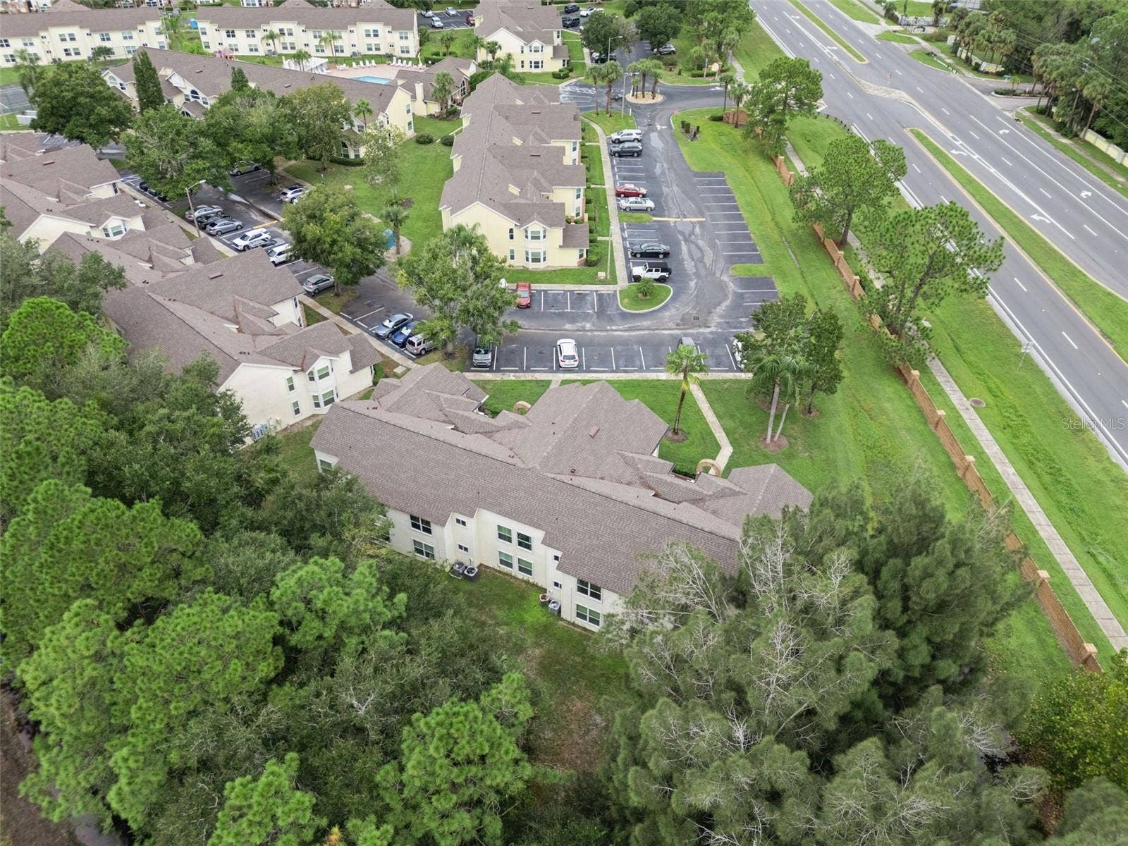 5017 LAGUNA BAY CIRCLE, #100, Kissimmee, FL 34746 Rear Exterior Aerial: Overhead aerial perspective of the building's rear, showing rooflines, bordering pine tree conservation area, and neighborhood surroundings