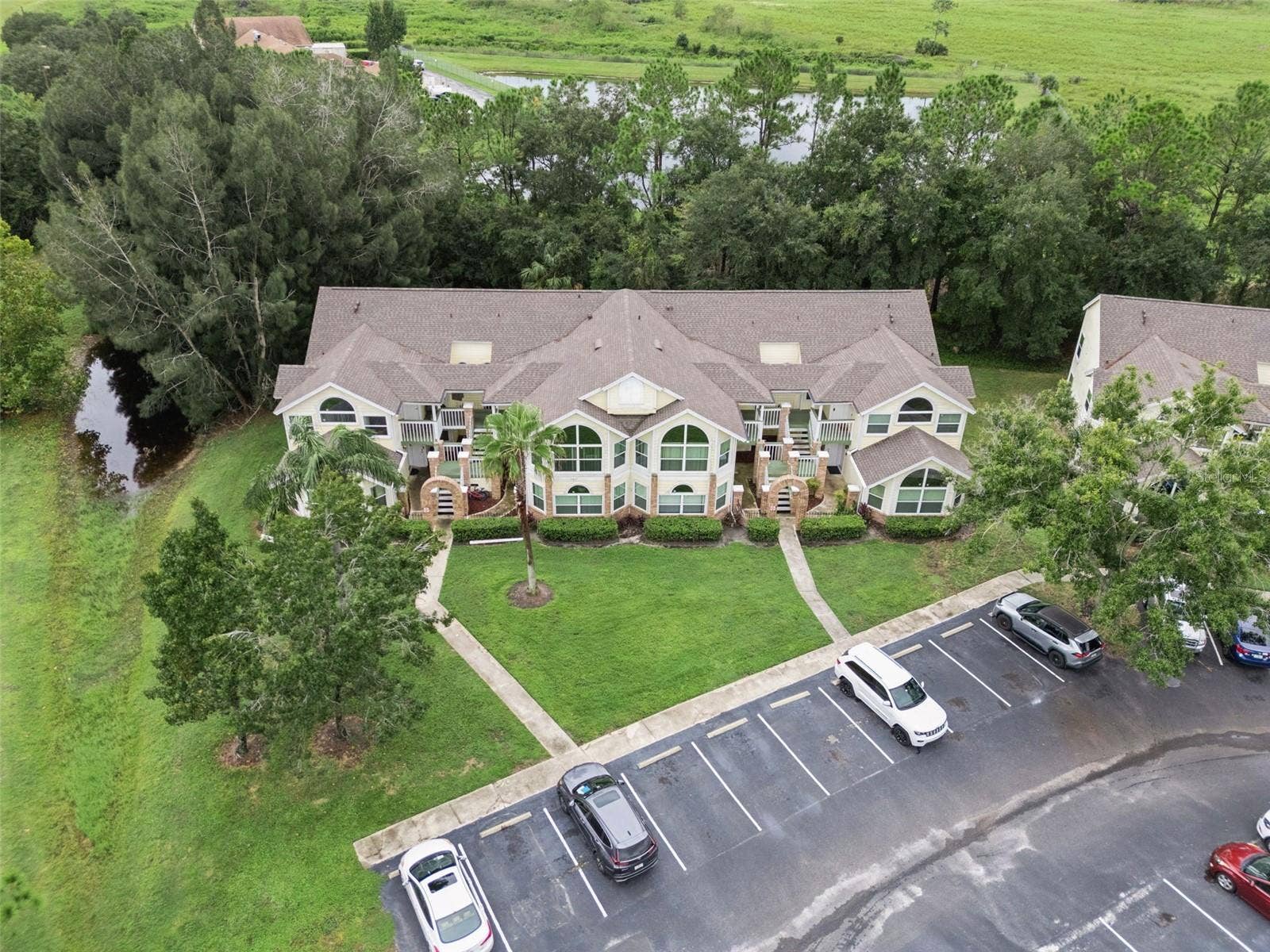 5017 LAGUNA BAY CIRCLE, #100, Kissimmee, FL 34746 Building Aerial Overview: Elevated drone shot showing the front building elevation, manicured lawn, and convenient resident parking spaces