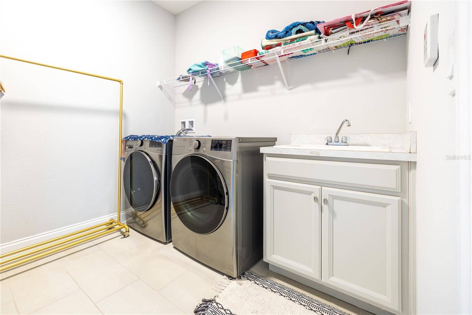 1316 SOUTHERN SUN DRIVE, Oakland, FL 34787 Laundry room with included front-load washer and dryer, utility sink, and storage shelving.