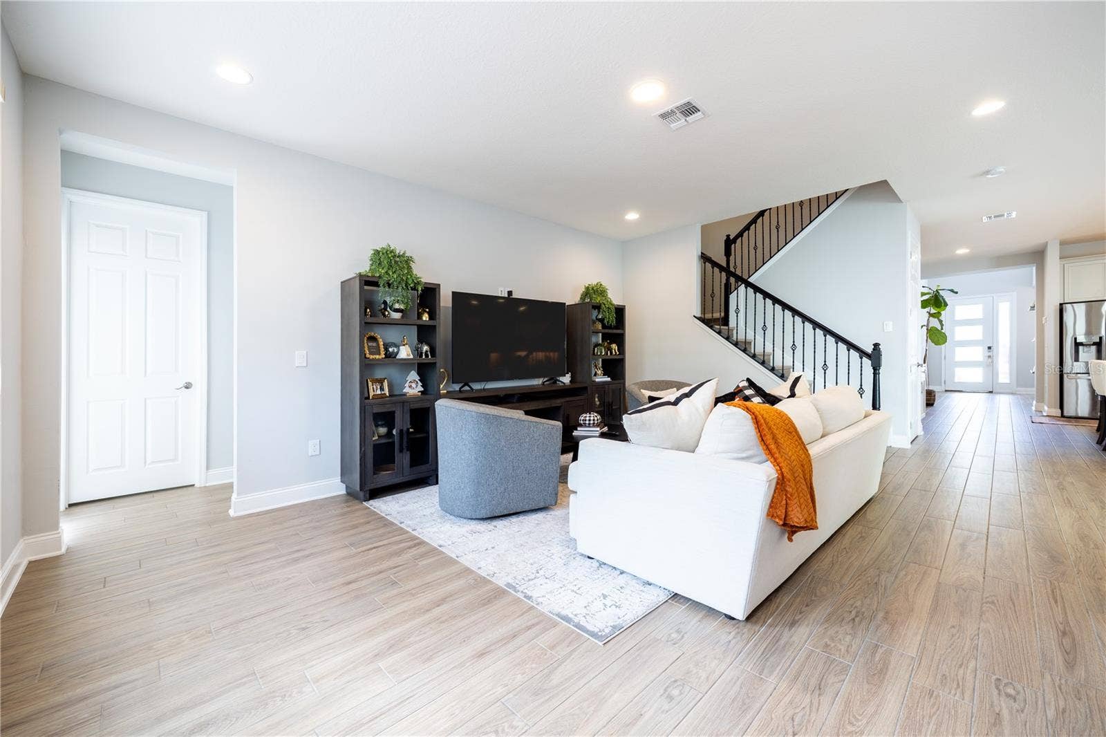 1316 SOUTHERN SUN DRIVE, Oakland, FL 34787 Open-concept living room with wood-look tile flooring and a staircase with decorative metal railings.