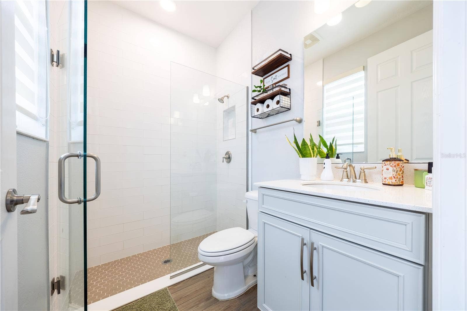1316 SOUTHERN SUN DRIVE, Oakland, FL 34787 Bright bathroom with a frameless glass shower, white tile, mosaic shower floor, and light blue vanity.