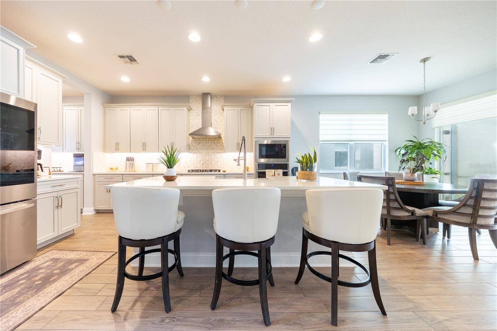 1316 SOUTHERN SUN DRIVE, Oakland, FL 34787 Spacious kitchen island with seating for three, complemented by white cabinetry and a decorative tile backsplash.