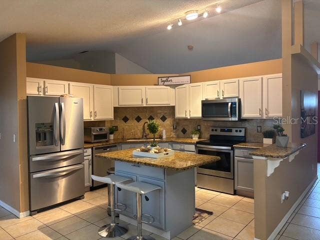 Kitchen view white cabinets with solid counters, island, stainless steel appliances, splash, and breakfast counter.