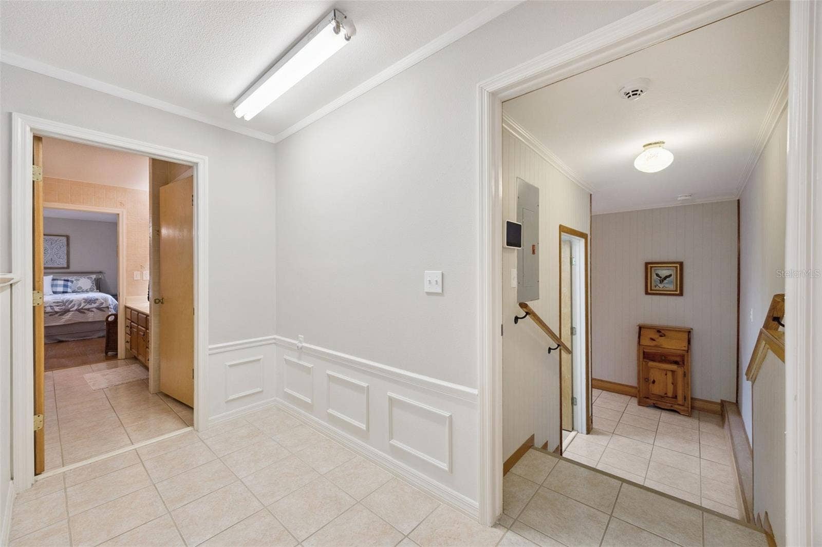 Split-Level Hallway Landing: Tiled split-level transition area featuring lower-level stair access, wainscoting wall detail, overhead lighting, and bedroom doorways.