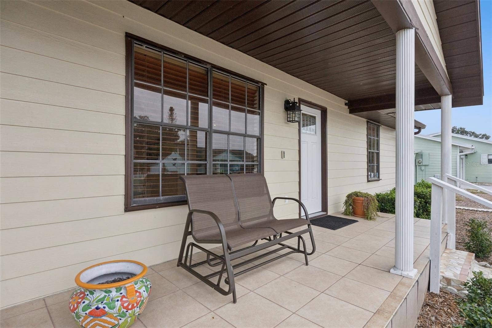 Porch Seating Area: Cozy front porch retreat with tiled floor, dark wood panel ceiling, and ample space for outdoor seating.