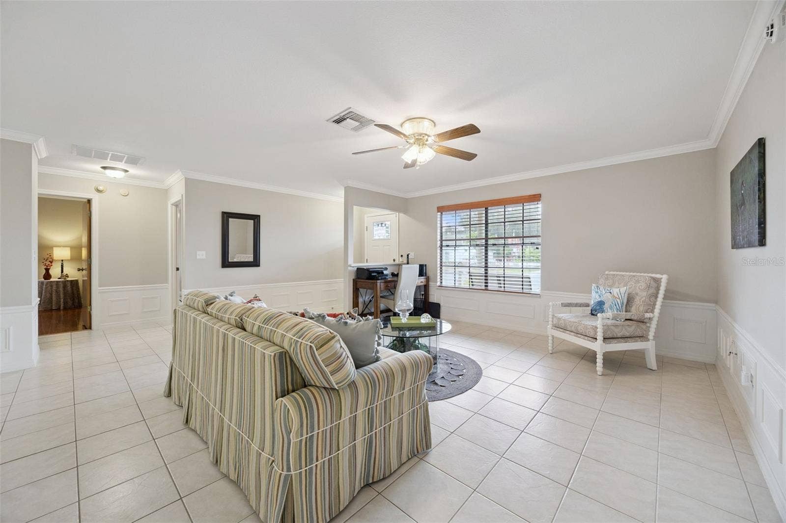 Living Room Corner: Comfortable living room layout showcasing light tiled floors, wall wainscoting, a ceiling fan, and views toward adjacent entry areas.