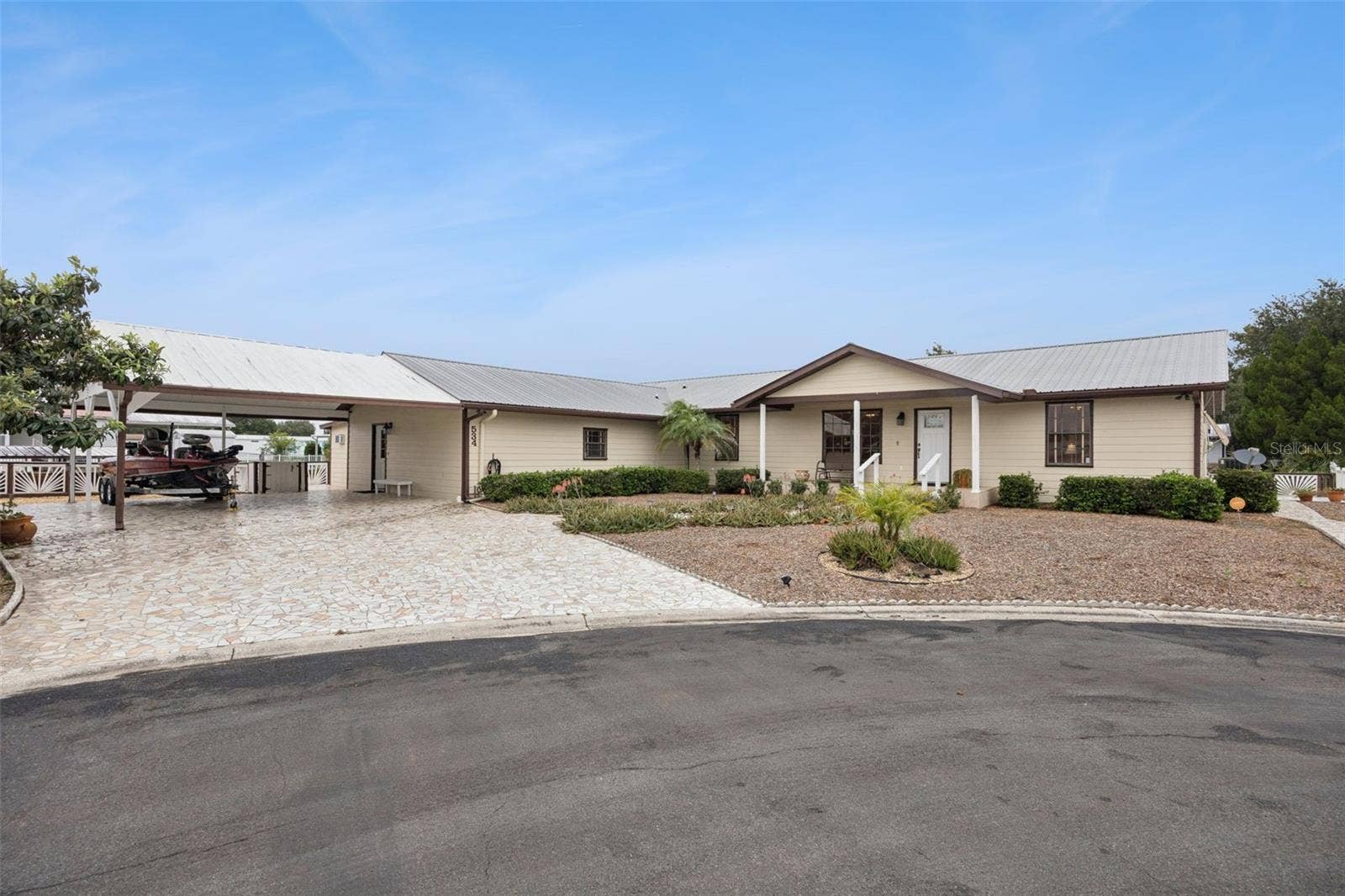 Front Elevation & Carport: Wide front perspective showcasing the extended stone driveway, large attached double carport, covered front porch, and manicured xeriscape landscaping.