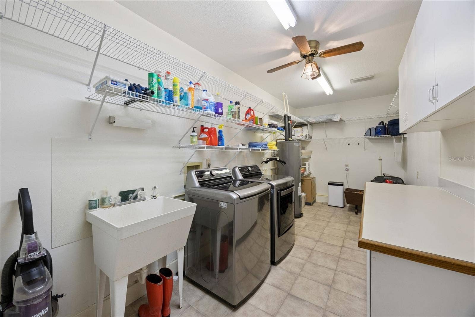 Dedicated Laundry Room: Large utility room featuring a laundry sink, side-by-side washer and dryer, water heater, overhead storage wire racks, and upper cabinets.