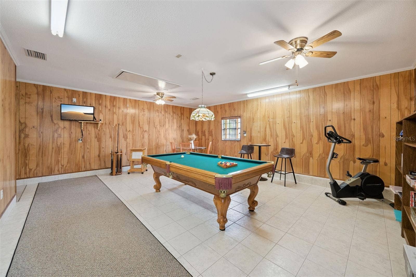 Recreation Room Perspective: Broad view of the expansive game room detailing wood-paneled walls, tile floors, hanging Tiffany-style billiard light, and flexible space for entertainment.