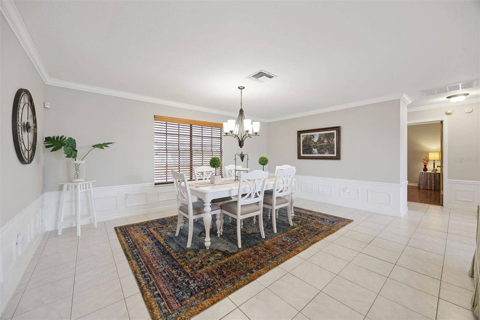 Formal Dining Room: Elegant formal dining area featuring classic wainscoting paneling, crown molding, a central chandelier fixture, and tiled flooring.