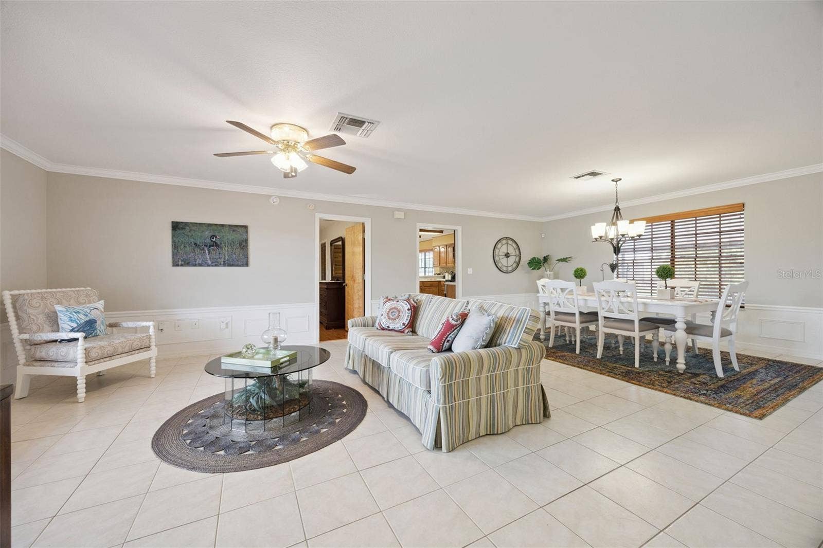 Formal Living & Dining View: Expansive great room highlighting tile flooring, detailed wainscoting, ceiling fan, and open flow into the formal dining space.