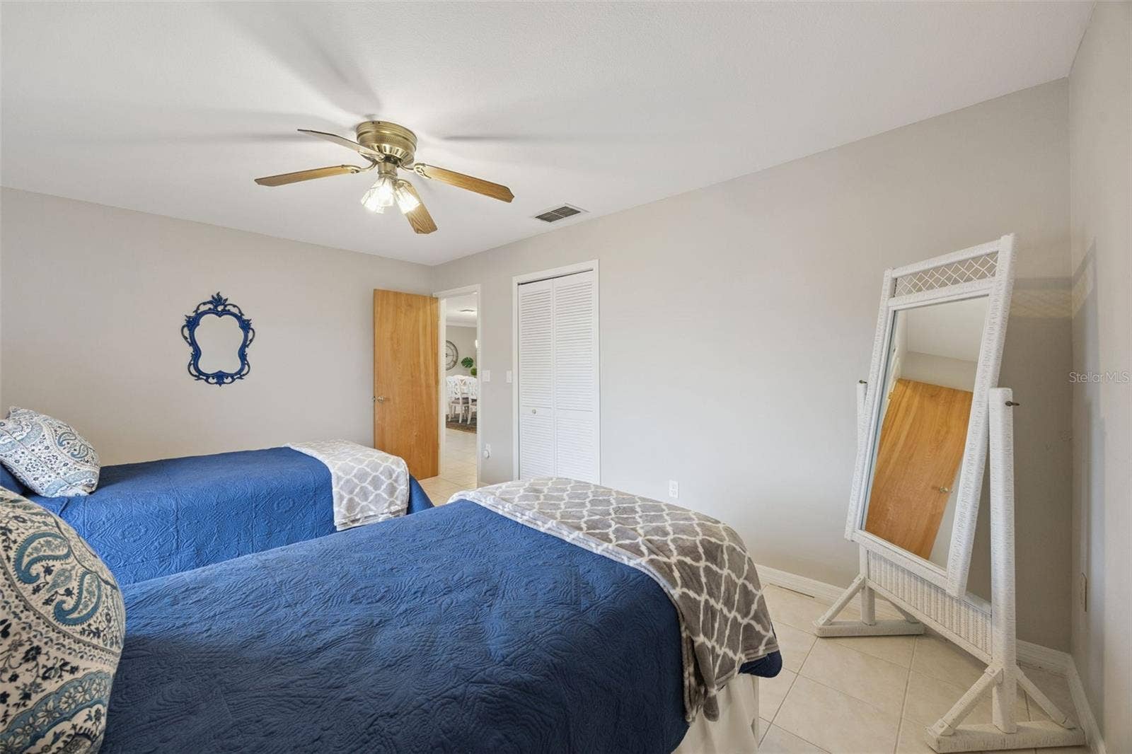 Twin Guest Bedroom: Spacious guest bedroom setup with dual twin beds, neutral tiled flooring, ceiling fan, and louvered closet doors.