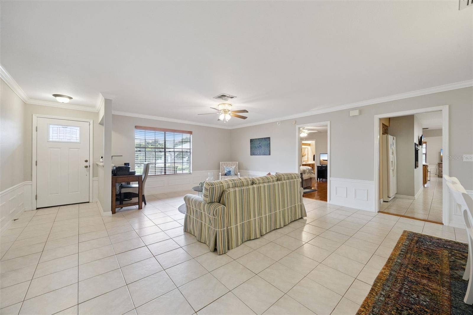 Open Living Room Flow: Expansive view across the living room featuring tiled flooring, crown molding, front entrance door, and hallway connections.