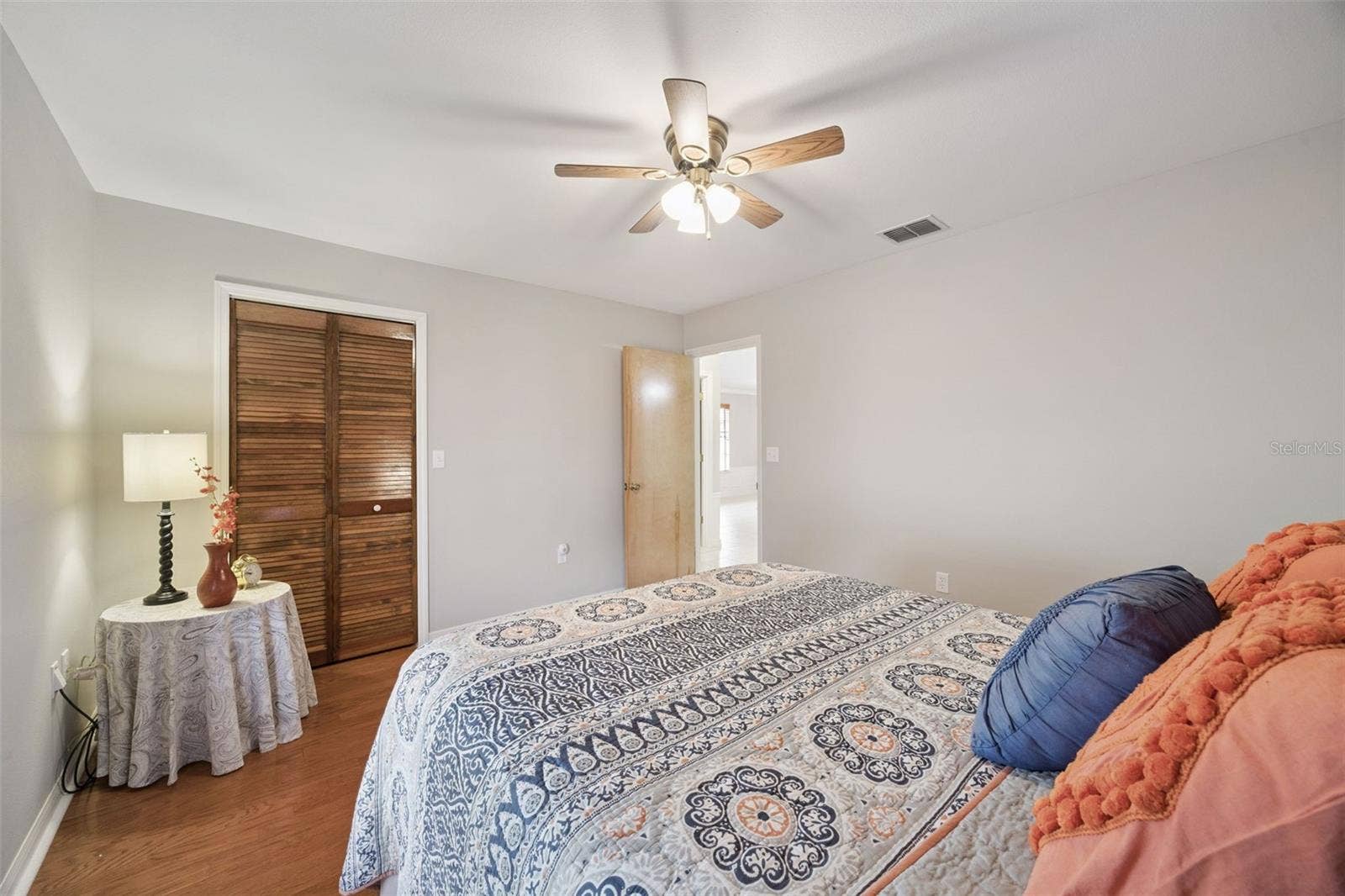 Guest Bedroom Closet: Comfortable secondary bedroom showing warm wood flooring, ceiling fan, and a built-in louvered closet.