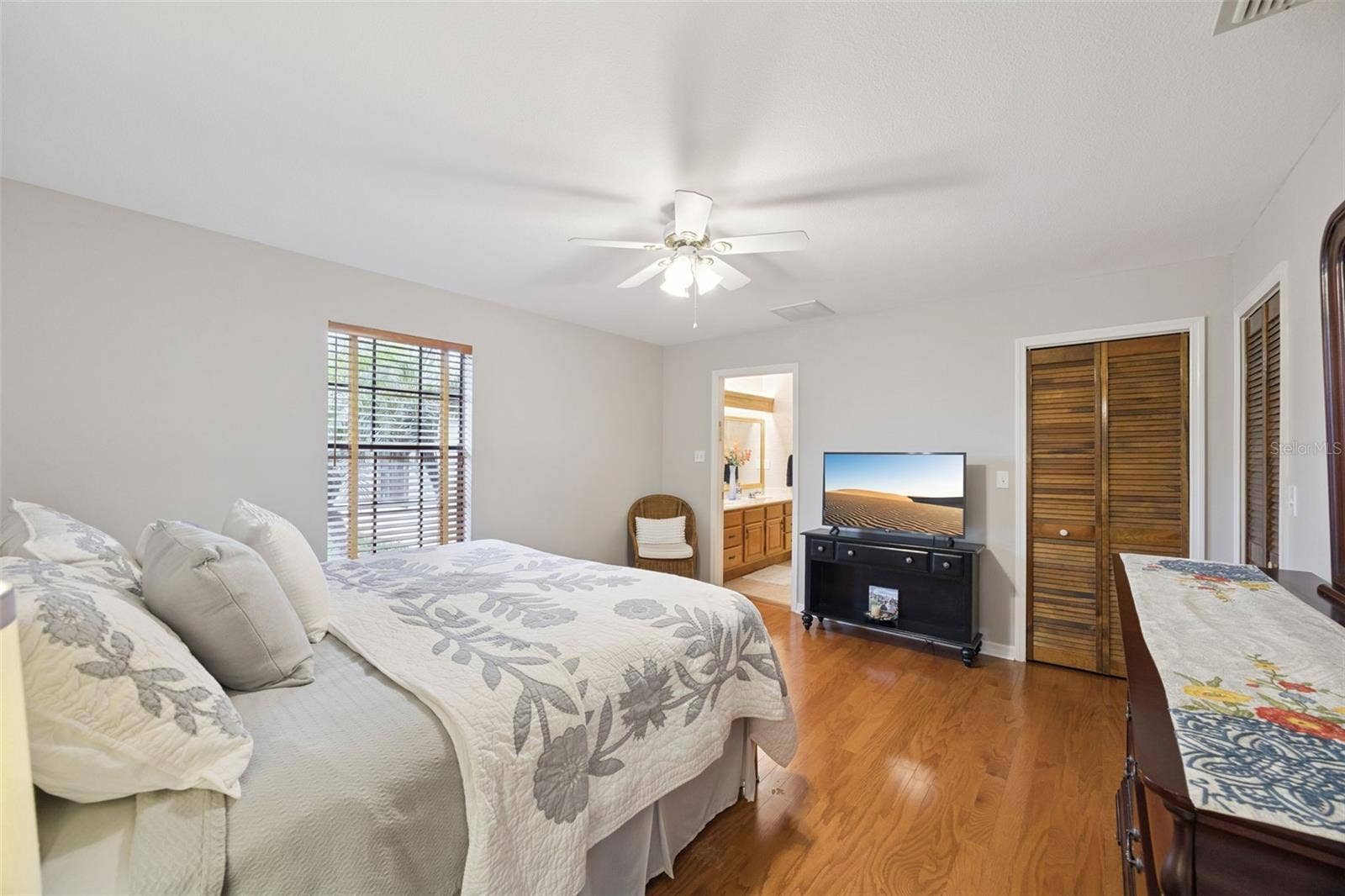 Primary Bedroom Suite: Spacious primary bedroom featuring warm wood laminate flooring, ceiling fan, louvered closet doors, and access to an ensuite bathroom.