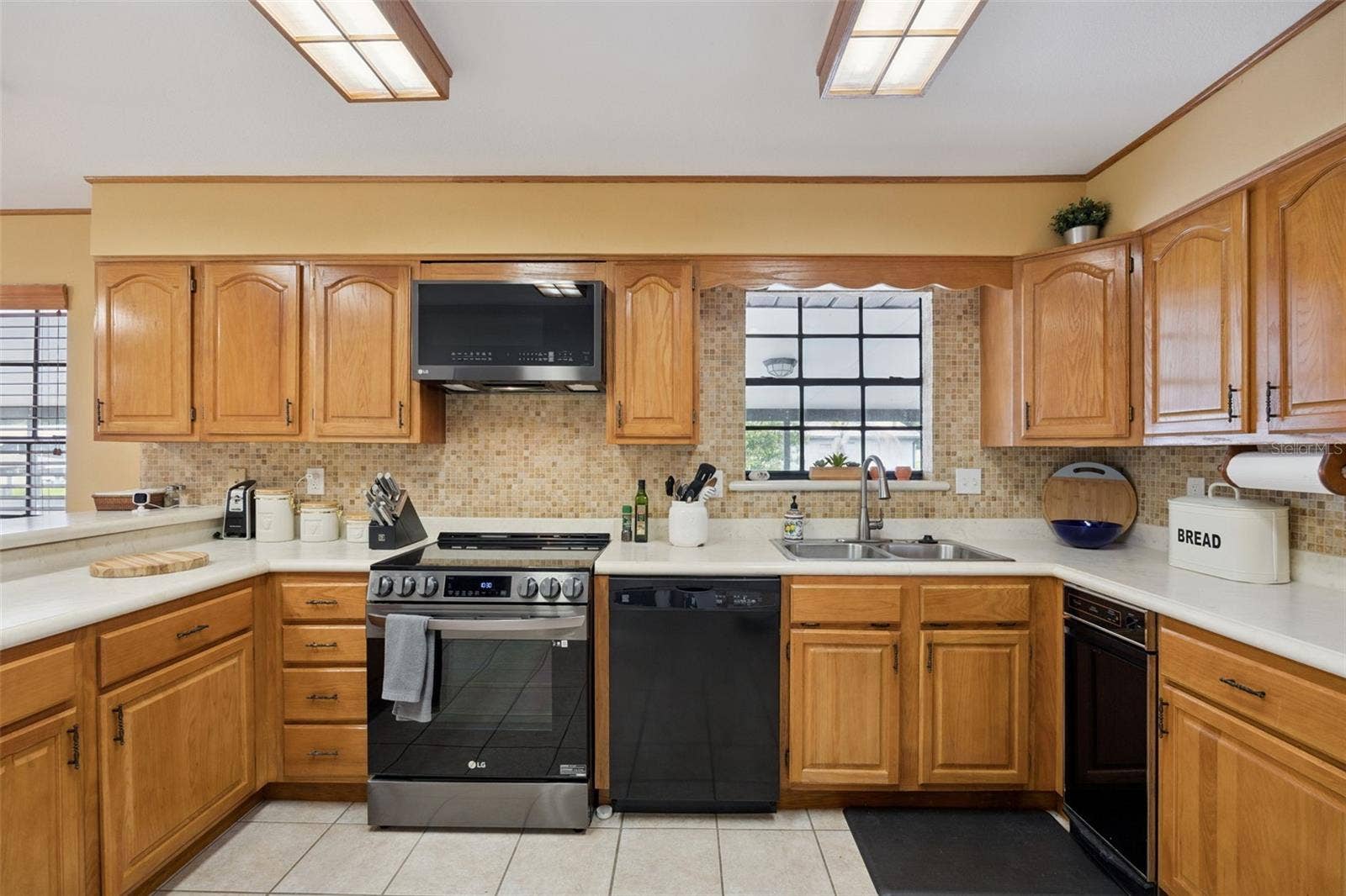 Centered Kitchen Suite: Direct view of the kitchen workspace featuring a double-bowl sink, electric range with microwave hood, dishwasher, and warm wood cabinetry