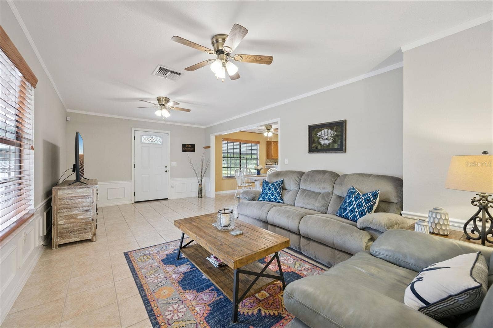 Living Room Perspective: Light-filled family room showing a seamless transition to adjacent living spaces, complete with neutral walls, ceiling fans, and large picture windows.
