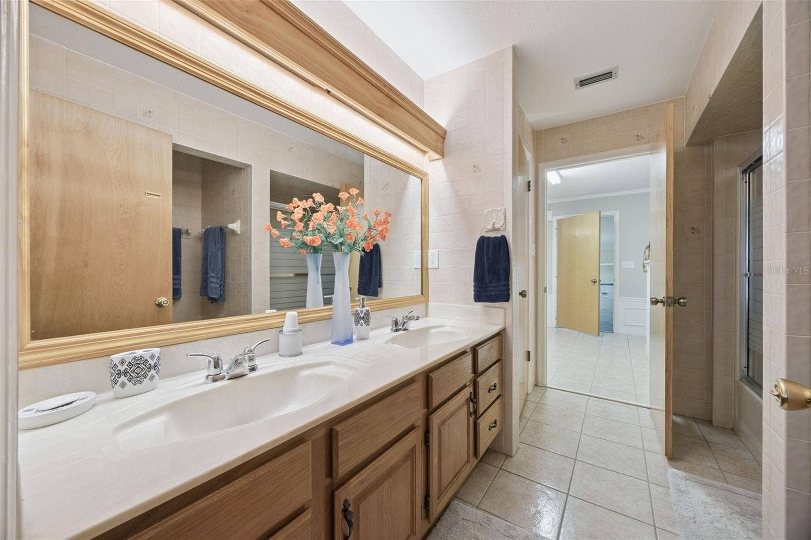 Dual Sink Primary Vanity: Long primary bathroom vanity with double sinks, warm wood cabinetry, full-width mirror, and integrated lighting.