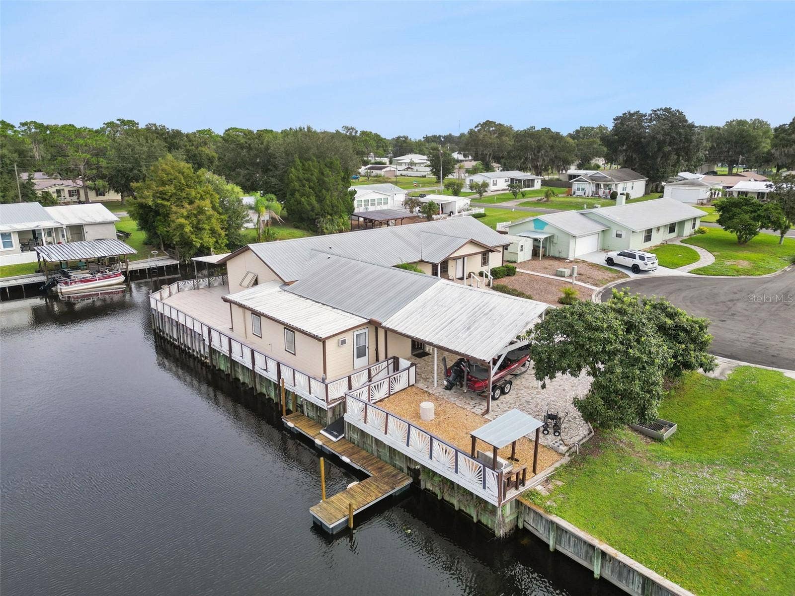 Aerial Side View & Boat Slip: Drone photo capturing the property's side dock, trailered boat carport, gravel patio area, and direct canal frontage