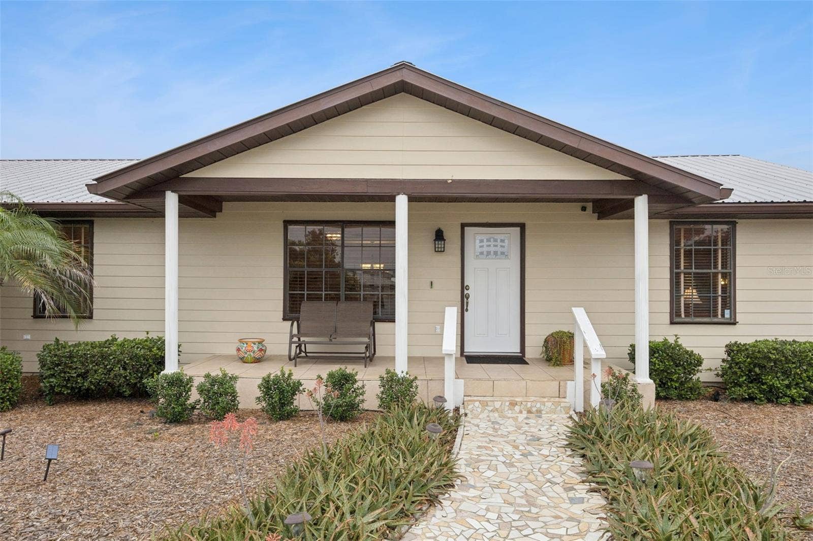 Covered Front Entry: Inviting covered front porch with decorative white support columns, tile flooring, and custom stone pathway leading to the main door.