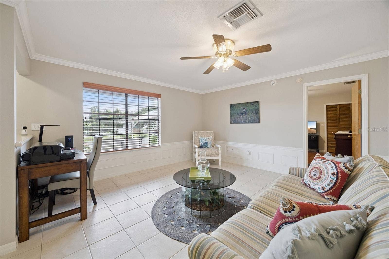 Living Room Workspace: Living area overview highlighting a dedicated desk nook along a half wall, ceramic tile flooring, and natural light from a large front window.