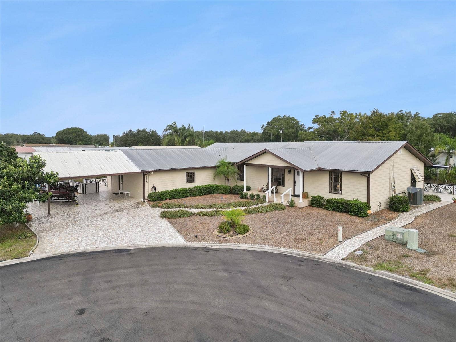 Aerial Front Street View: Elevated view highlighting the spacious lot, wide cul-de-sac positioning, long stone driveway, and generous covered parking space.