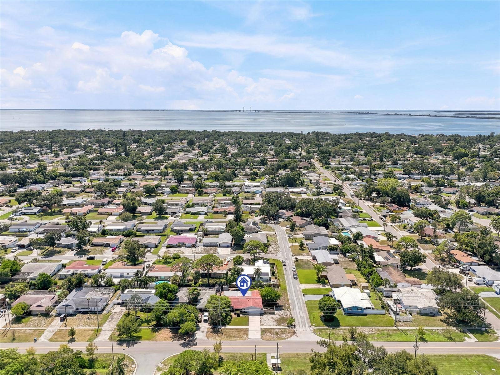 1890 62ND AVENUE S, St Petersburg, FL 33712 A wider aerial perspective places the home within its leafy St. Petersburg neighborhood, with the bay and Sunshine Skyway Bridge on the horizon.