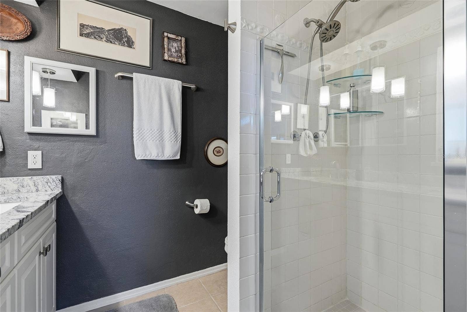 1890 62ND AVENUE S, St Petersburg, FL 33712 The primary bath features a glass-enclosed shower with classic white tile, glass corner shelves, and a convenient handheld showerhead.