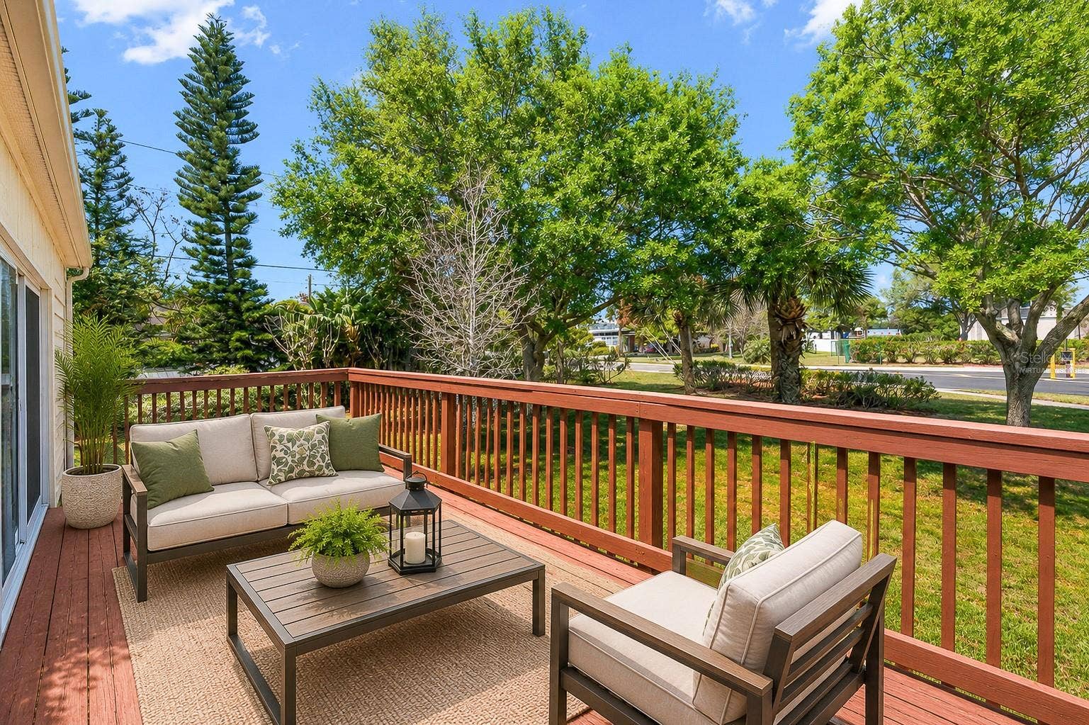Elevated deck with open railing overlooks a green, tree-lined setting, providing a sense of space and a pleasant outdoor backdrop. This photo has been virtually staged.