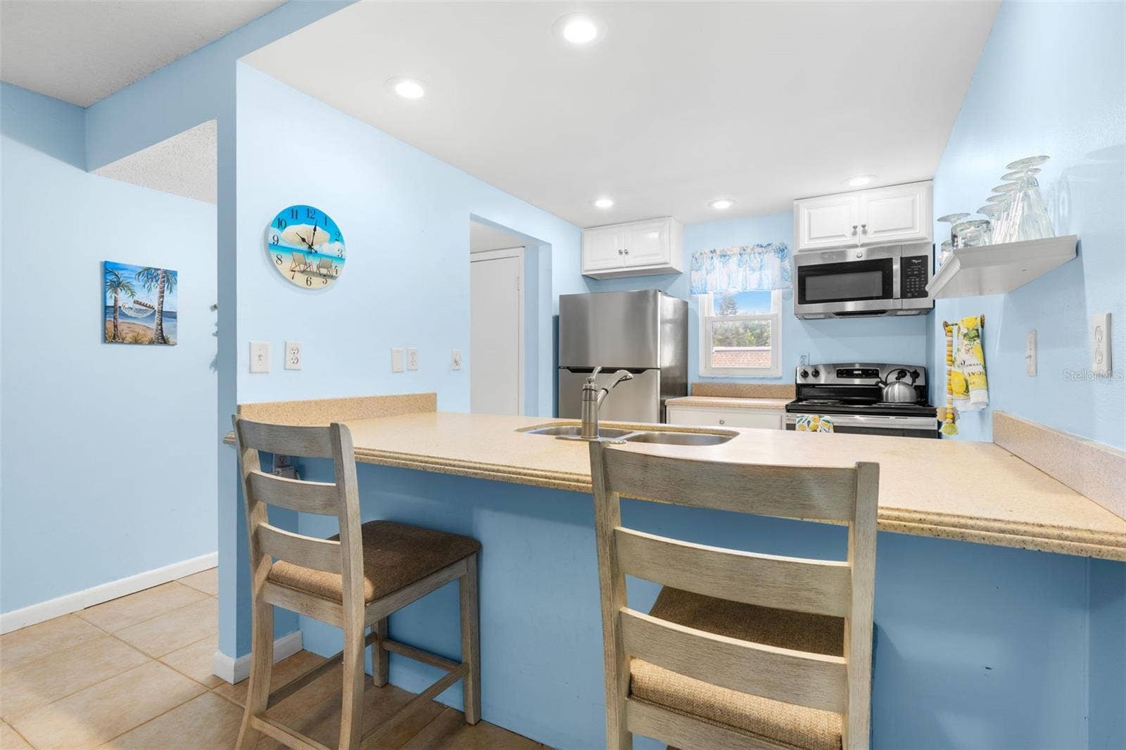 12760 INDIAN ROCKS ROAD, #107, Largo, FL 33774 The kitchen wraps around a broad Corian breakfast bar with seating for two, with recessed lighting, a window over the rear counter and stainless-steel appliances including the refrigerator, range and microwave.