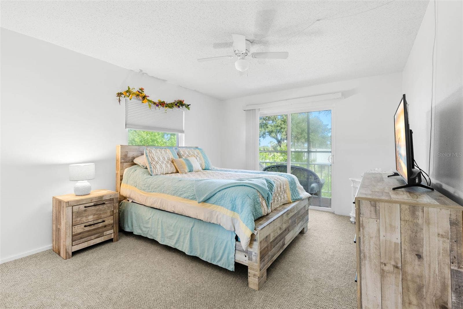 12760 INDIAN ROCKS ROAD, #107, Largo, FL 33774 A neutral backdrop of light walls and carpet keeps the primary bedroom bright, while a second window and sliding glass doors bring in natural light and frame the greenery outside.