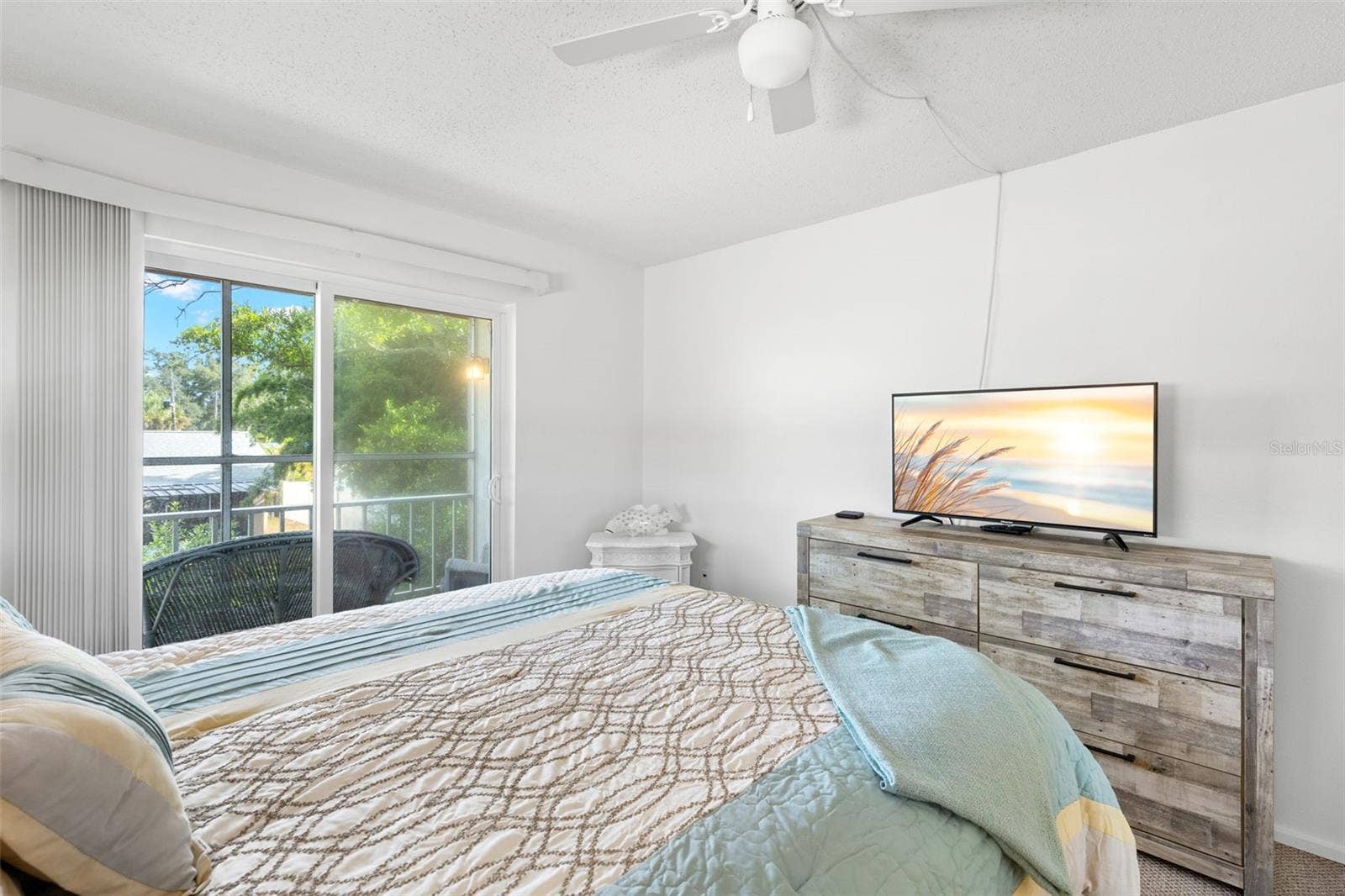 12760 INDIAN ROCKS ROAD, #107, Largo, FL 33774 The primary bedroom measures approximately 14'9" x 11'3", with a ceiling fan overhead and sliding glass doors opening directly to the screened balcony and its leafy outlook.