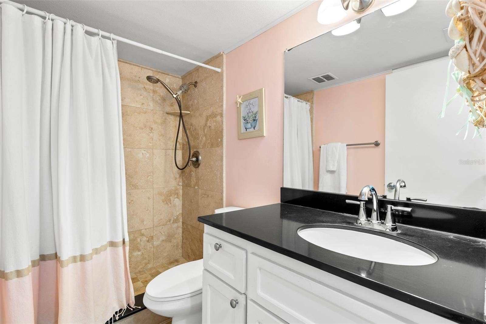 12760 INDIAN ROCKS ROAD, #107, Largo, FL 33774 The bath pairs a dark countertop with light cabinetry and a large mirror, while the tub/shower is finished with tile surround and a handheld showerhead.