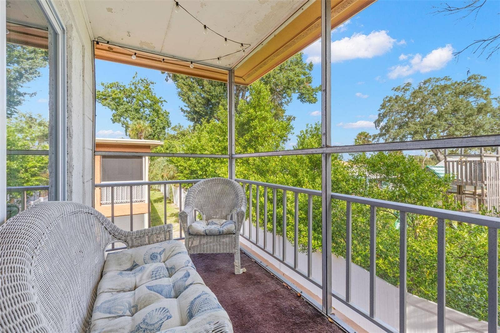 12760 INDIAN ROCKS ROAD, #107, Largo, FL 33774 The screened balcony extends the living space outdoors, with room for seating and a leafy outlook framed by mature trees and open sky.