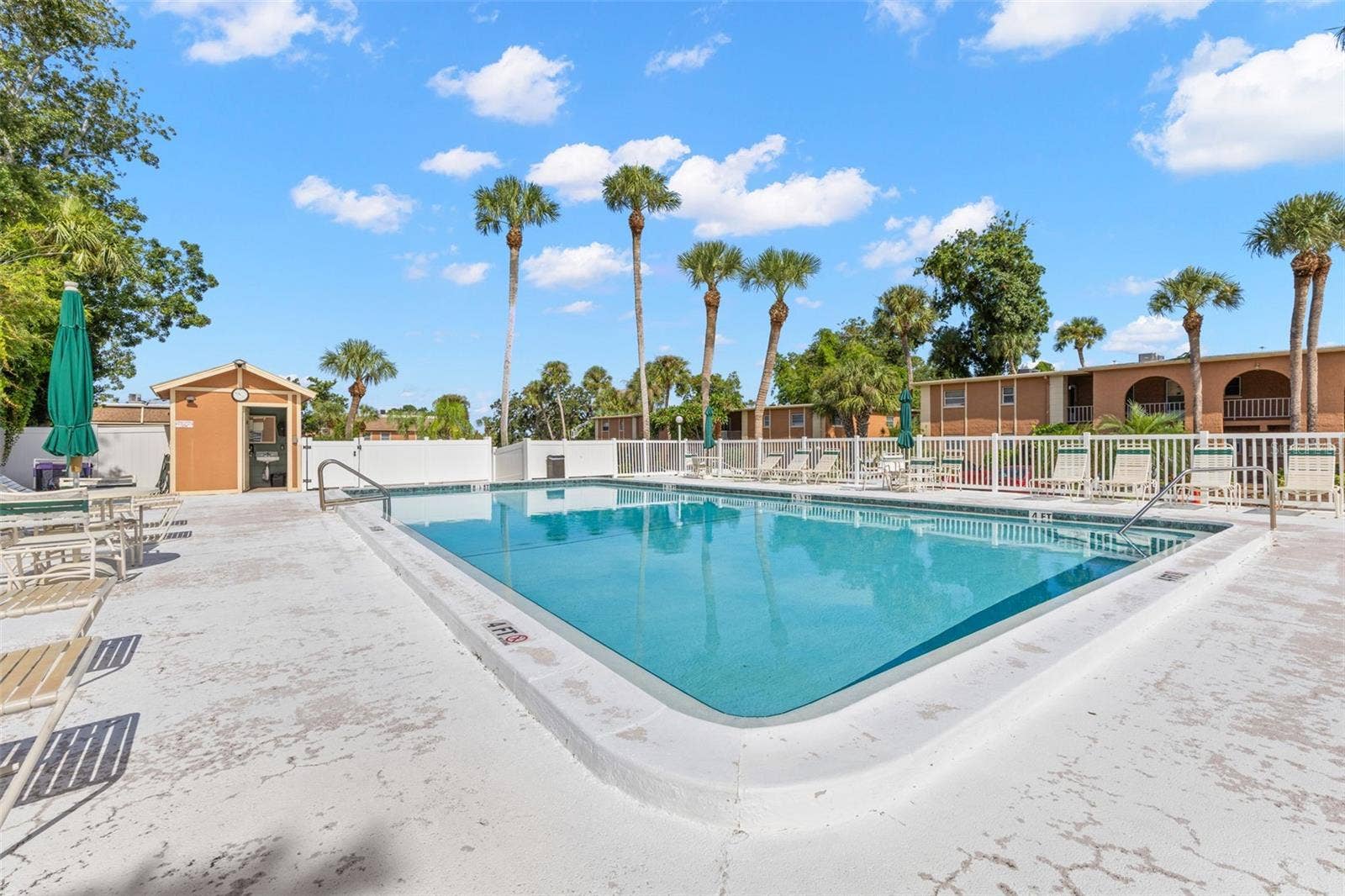 12760 INDIAN ROCKS ROAD, #107, Largo, FL 33774 One of the community pools offers a spacious deck with plenty of lounge seating and umbrellas, framed by tall palms and the surrounding residential building.