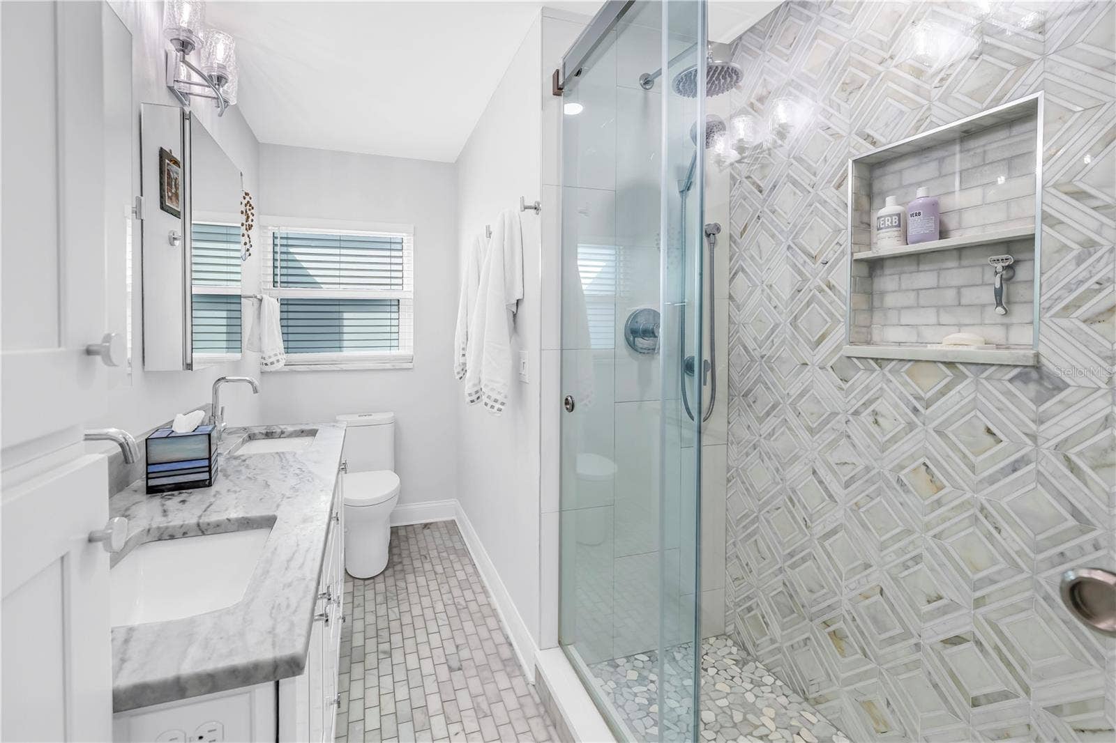 1114 2ND AVENUE S, Tierra Verde, FL 33715 Primary bath with designer shower with spa stones and Art Deco influenced sand and sea aesthetic and built- in shower niche.