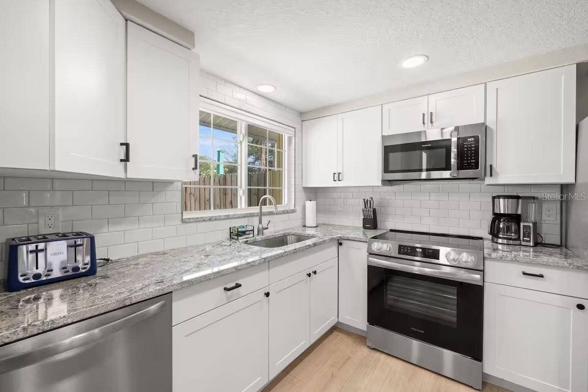 201 SOUTH STREET, Palm Harbor, FL 34683 Crisp white cabinetry, stainless steel appliances, granite counters, and subway tile create a bright, fresh kitchen with plenty of workspace and storage.
