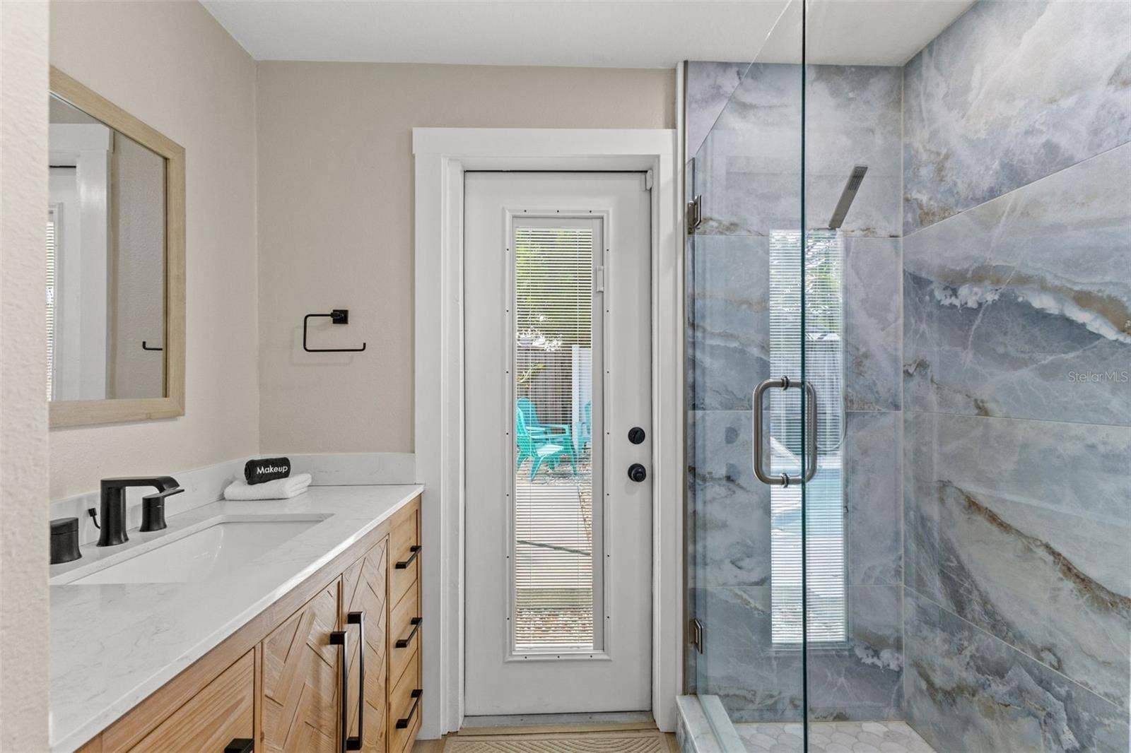 201 SOUTH STREET, Palm Harbor, FL 34683 Updated bath features a modern vanity, quartz-style countertop, black fixtures, and a striking glass-enclosed tiled shower.